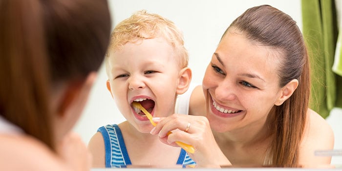 mother helps child brushing teeth