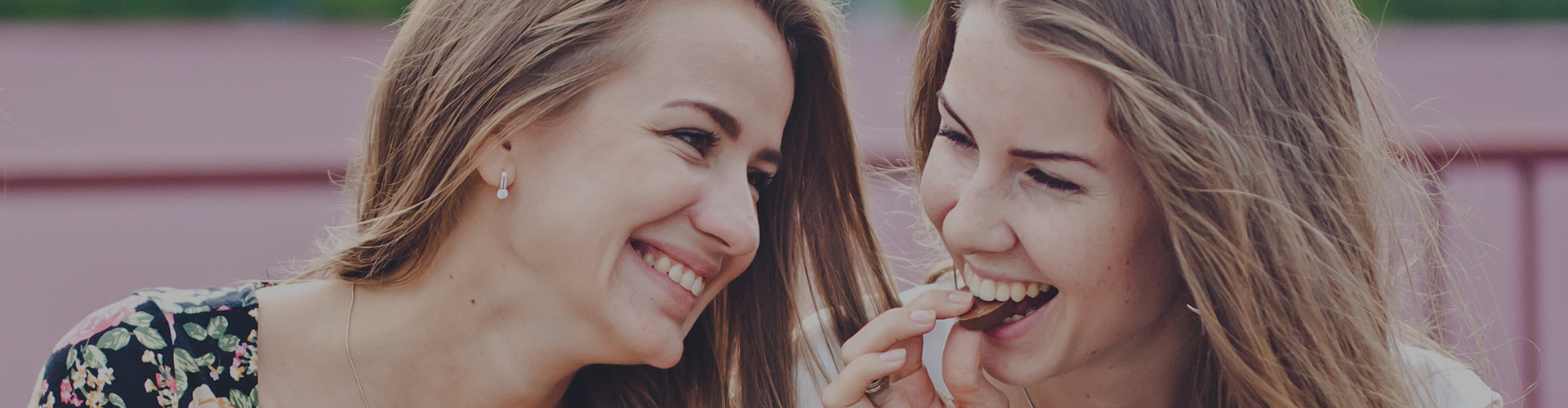 Two adult women with white teeth smiling while eating chocolate