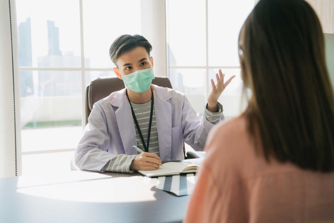 Dentist wearing mask talking to patient in diagnosis room